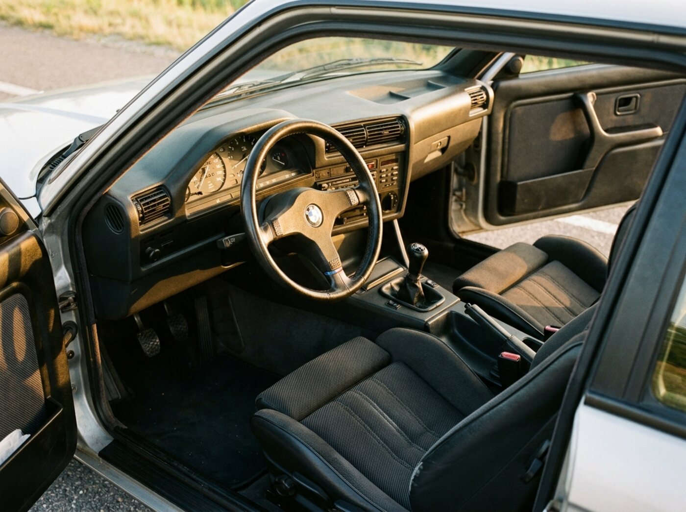 Intérieur BMW E30 : planche de bord orientée conducteur, volant sport trois branches, sièges sport tissu